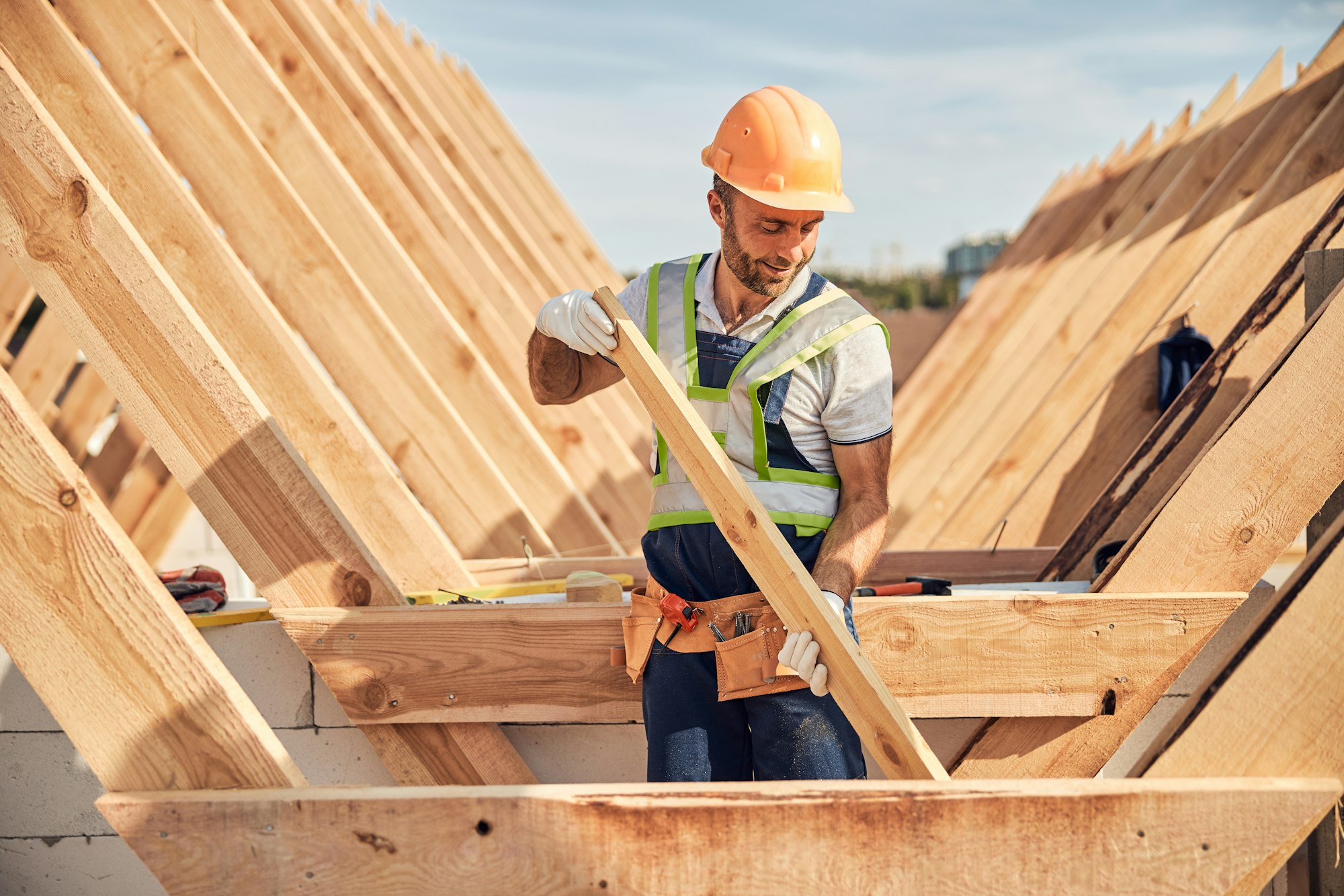 Focused builder is adjusting a wooden bar to a roof carcass