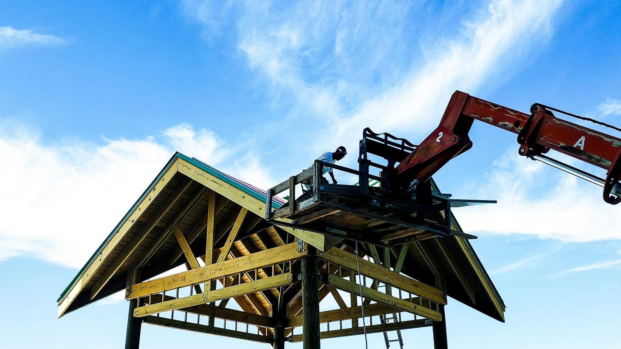 Mechanical crane lifts shingles up on rooftop for roofer to do his job.