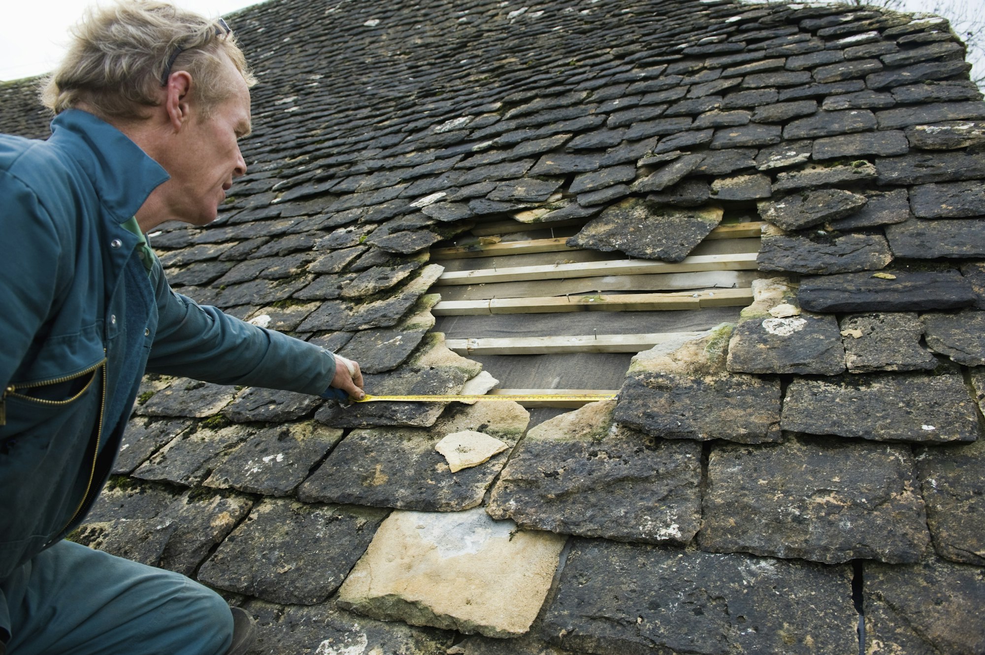 Roofer measuring hole in traditional stone tile roof